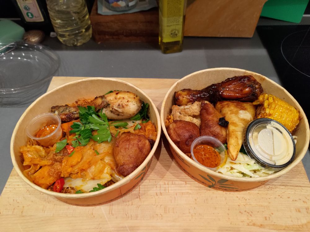 Två olika portioner god mat med bl.a. jollof rice, grillad kyckling, blomkål och majs, coleslaw, mikates och smarriga såser.