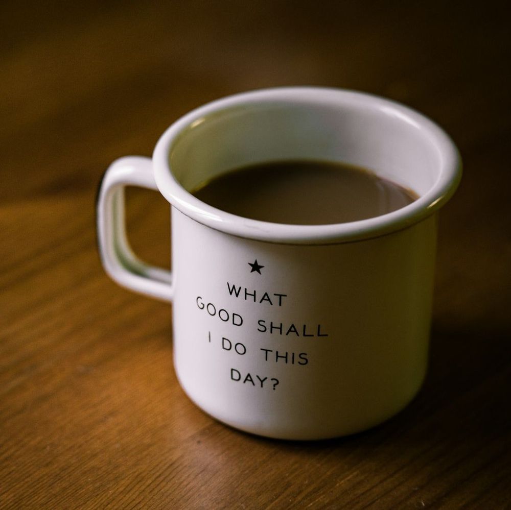 A coffee mug on a table that reads, "What good shall I do this day?"