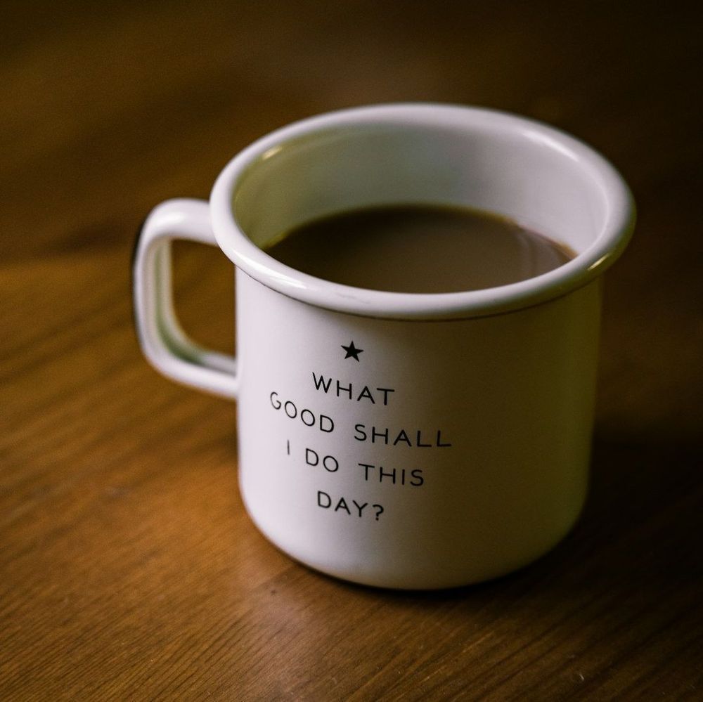 A coffee mug on a table that reads, "What good shall I do this day?"