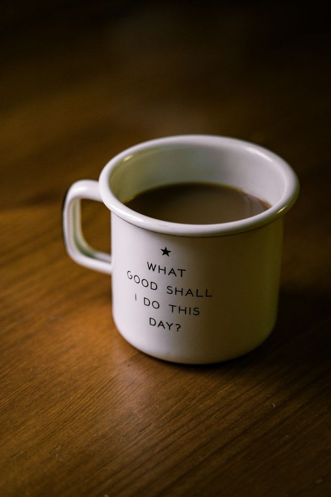 A coffee mug on a table that reads, "What good shall I do this day?"