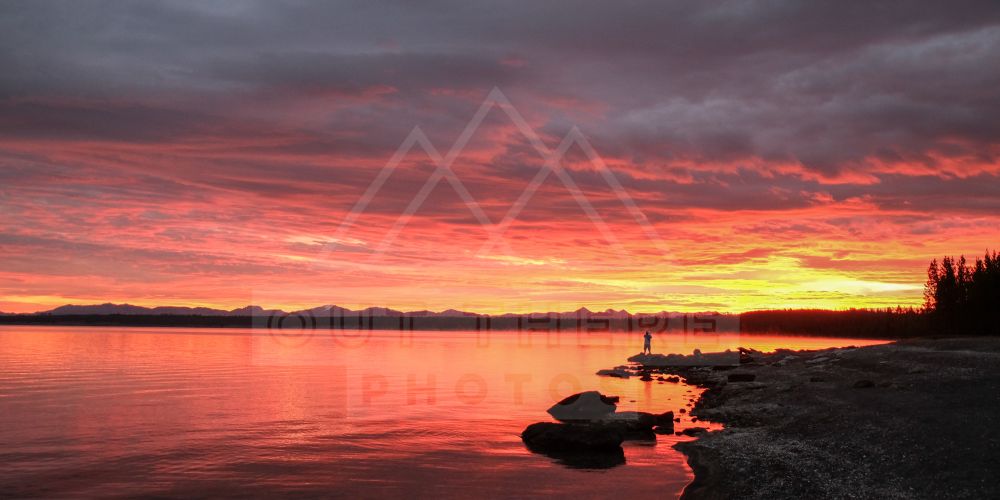 A vivid sunrise with red, orange, pink, and yellow tones in the sky, clouds, and reflected on the a lake 