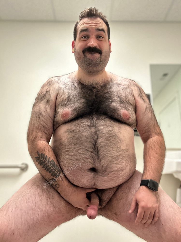 A hairy naked man with dark hairy and a mustache holding his hard cock