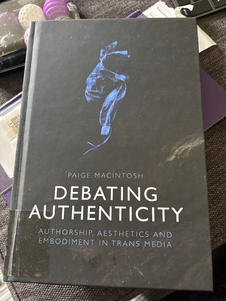 Hardcover book cover, dark with some abstract lighter shadows. It reads 'PAIGE MACINTOSH
DEBATING AUTHENTICITY AUTHORSHIP, AESTHETICS AND EMBODIMENT IN TRANS MEDIA’