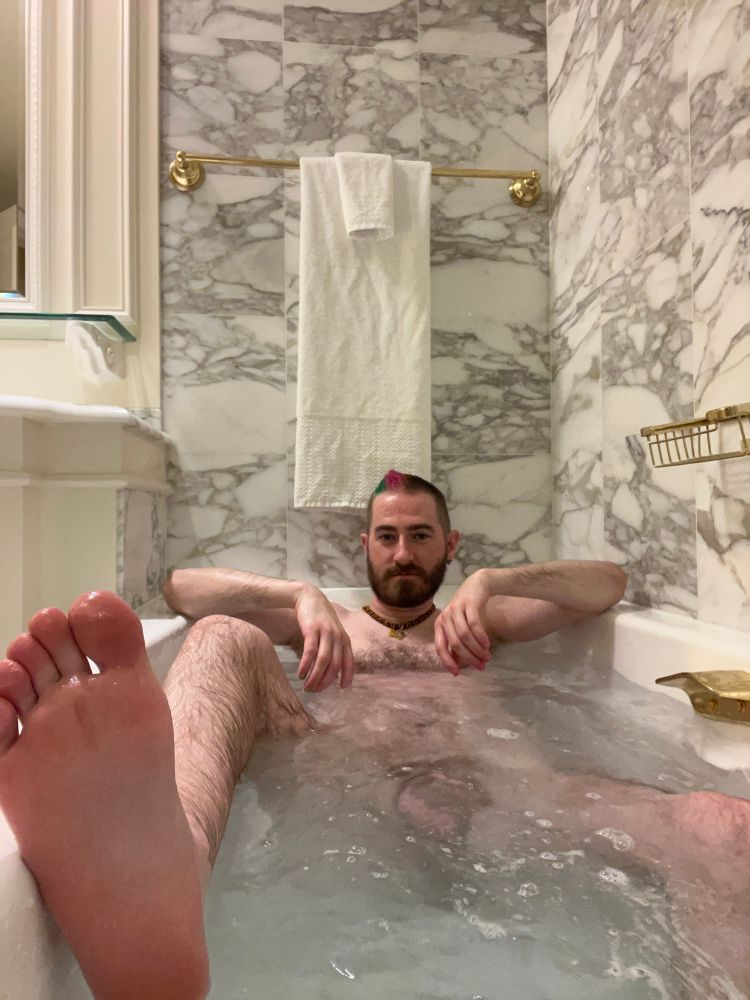 Me in a fancy bathtub with one foot up out of the water resting by the camera