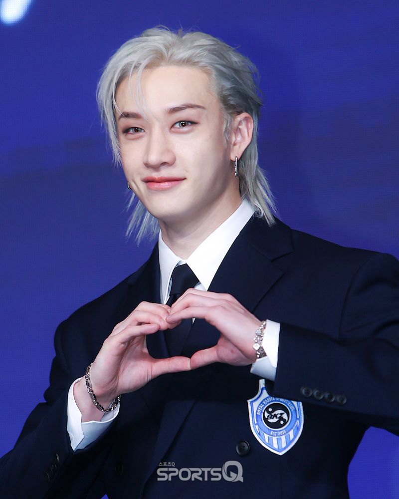 Photo by SportsQ. Chan with silver hair and wearing a black suit, he’s making a heart with both hands