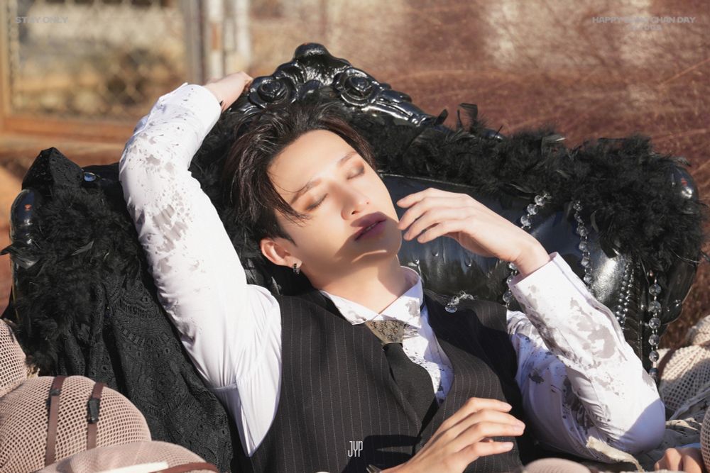 Chan sitting in an armchair. He’s outside, with the sun over him. He has his eyes closed, one hand is touching the back of the armchair, and the other is near his face.