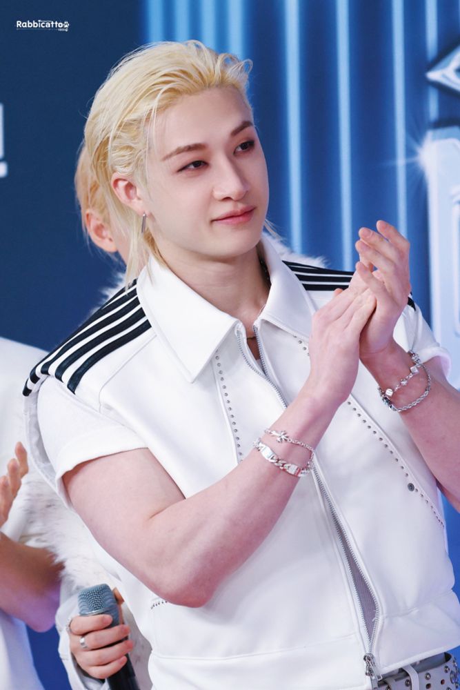 Chan clapping his hands. He’s wearing white clothes with black details on the shoulder.