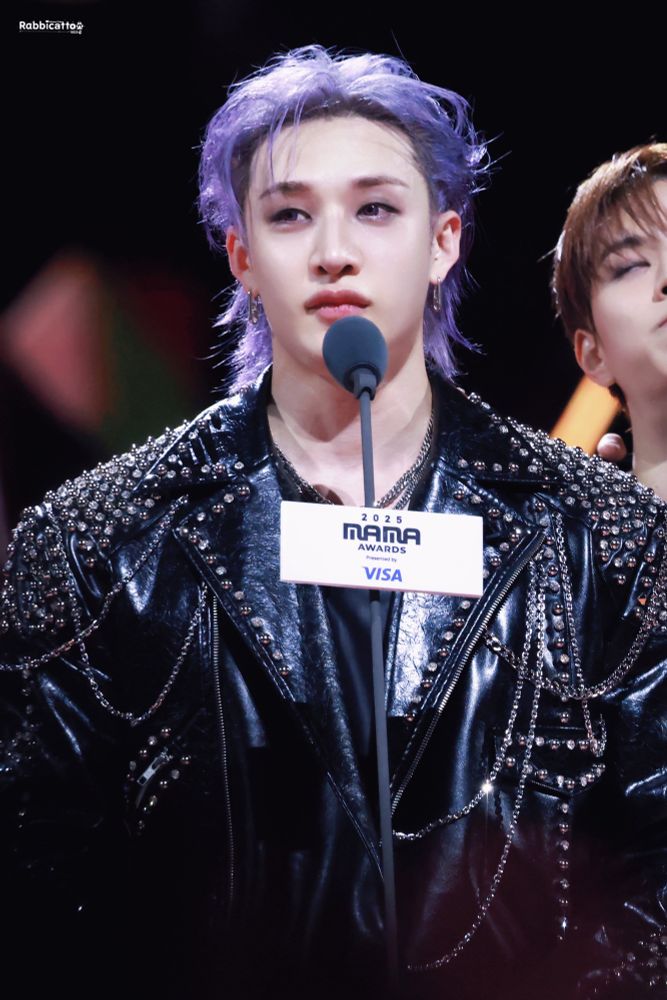 Chan talking in the mic for the MAMA Awards. He’s wearing black clothes, and with purple hair