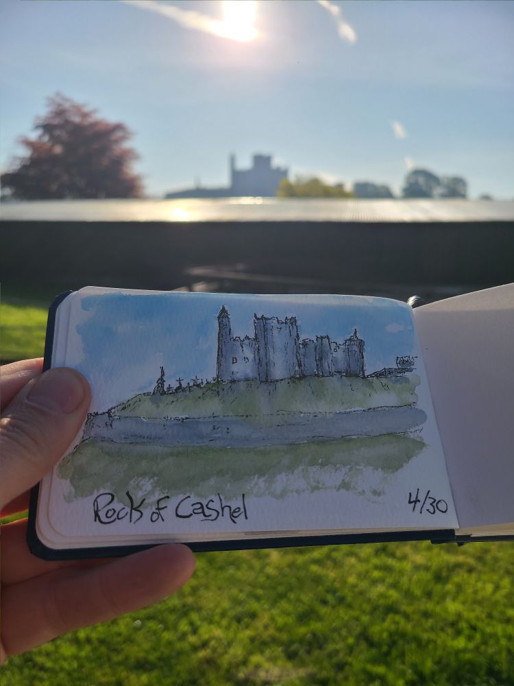 An ink and wash sketch of the rock of Cashel silhouetted against morning sun is held up against the actual view.