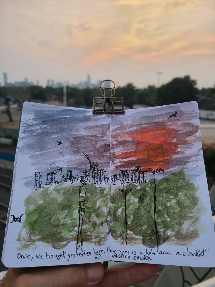 A sketchbook is held up in front of the scene depicted. An orange setting sun is obscured by wildfire smoke. In the foreground parking lot lights and a cell tower stand in front of trees and a cityscape. Karma's a bitch, ain't it?