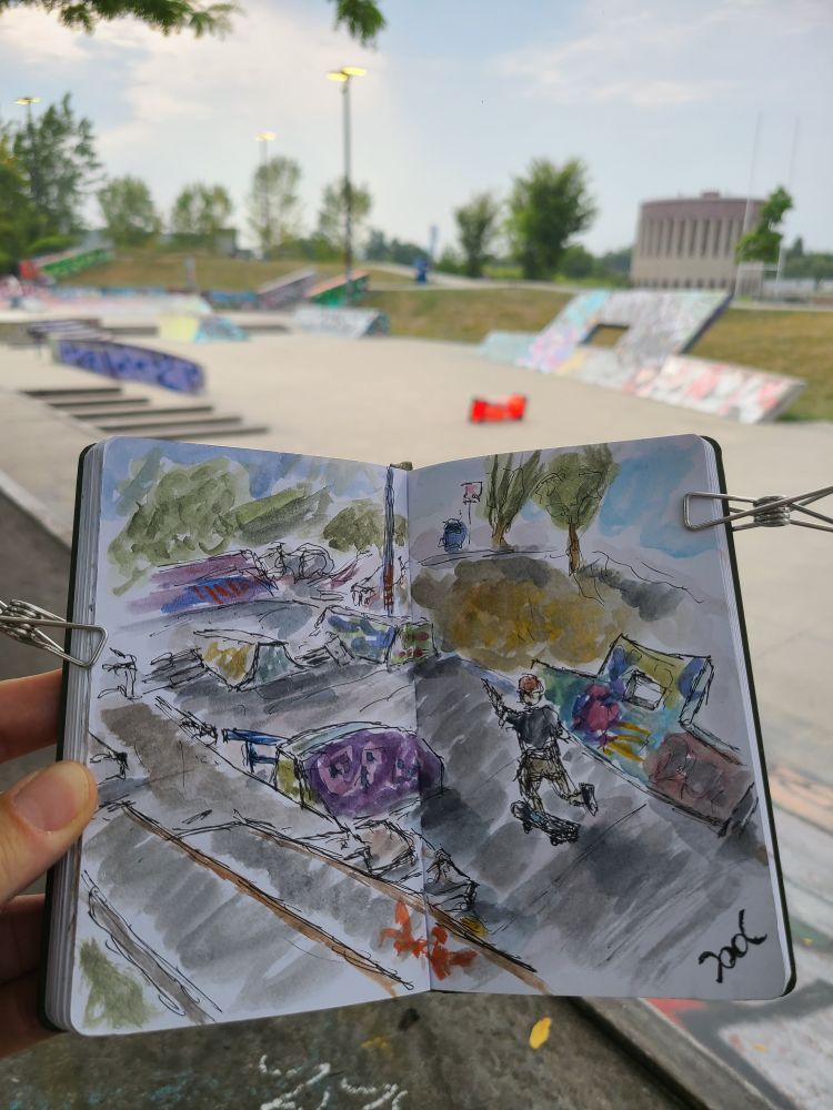 A sketchbook is held up in front of the scene depicted. A skateboarder rolls through a graffitied skatepark with many features and obstacles. Some trees are visible in the distance. That thing they say about doing one thing a day thay scares you? It's worth it to feel really alive!