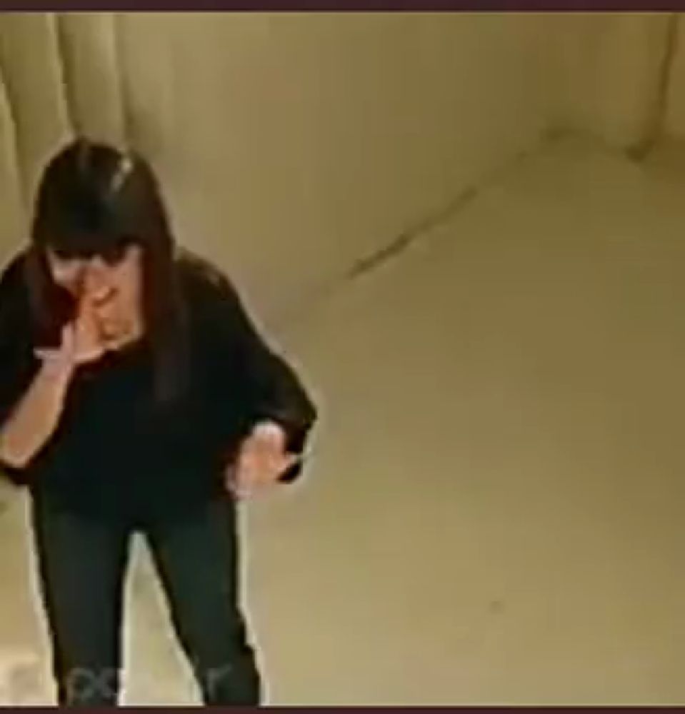 a woman in a black shirt and black pants is standing in a room and smoking a cigarette .