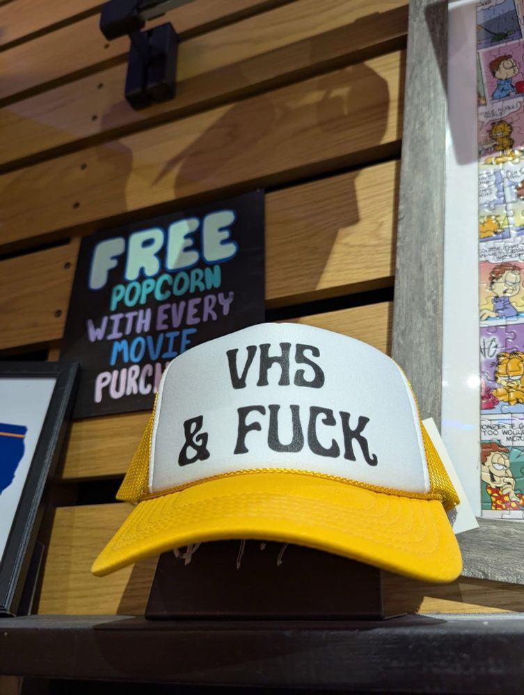 A trucker cap sitting on a counter proudly stating in large font, “VHS & FUCK”