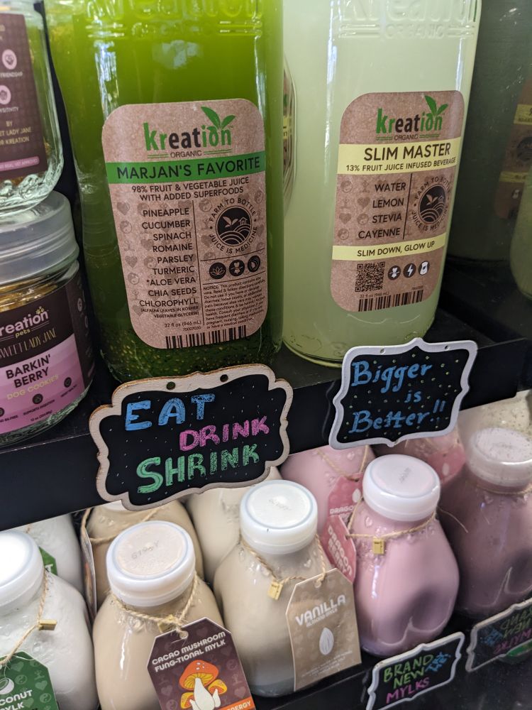 Health drinks with a pair of signs that say "eat drink shrink" and "bigger is better"