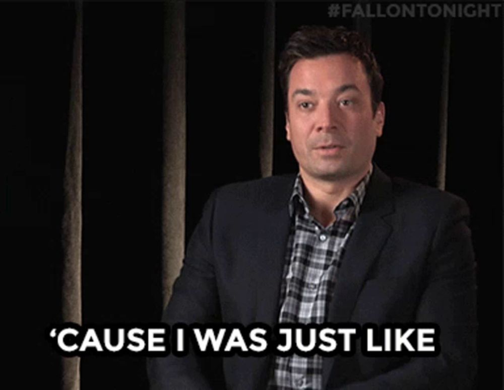 a man in a suit and plaid shirt is waving his hand in front of a black curtain with #fallontonight written on it