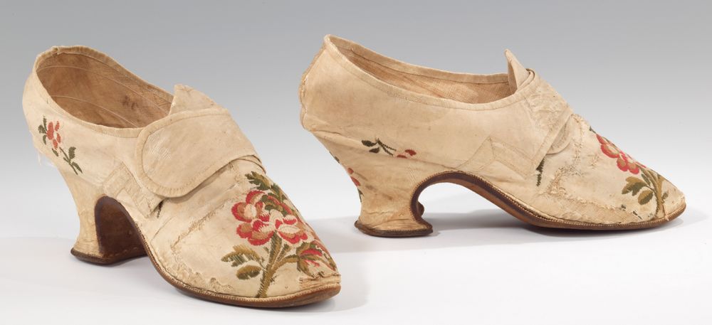 A pair of shoes made of white silk brocaded in pinks and greens with flowers, stems, and leaves, the silk cut so that large flowers are over the vamps. Latchets for buckles are placed over the vamp. High, curved heels.