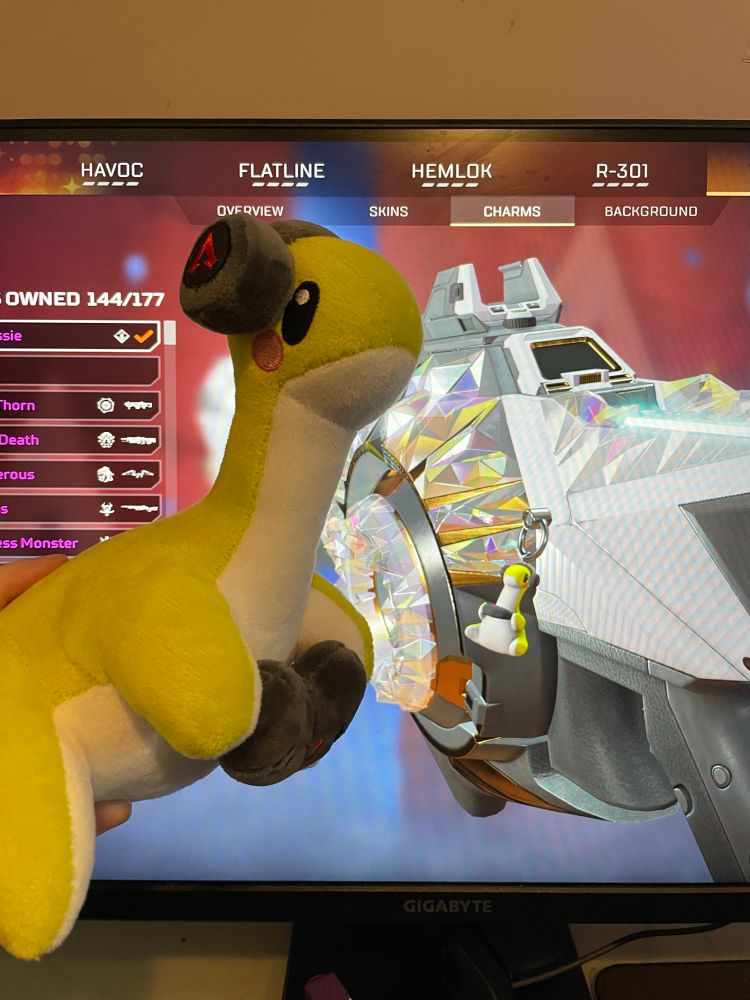 Picture of the gamer nessie plush in front of a monitor displaying the gamer nessie charm in game