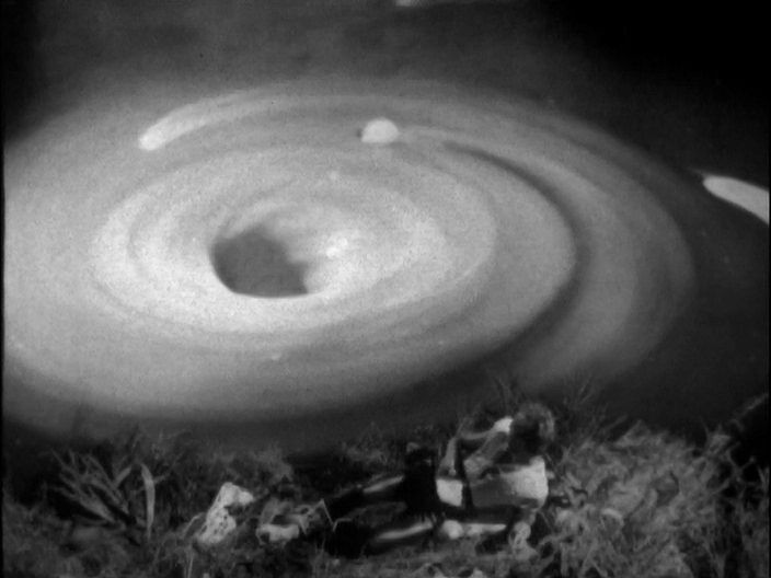 Ayldon at the bottom of the frame in some grass looks at a whirlpool with an eye wider around than he is.