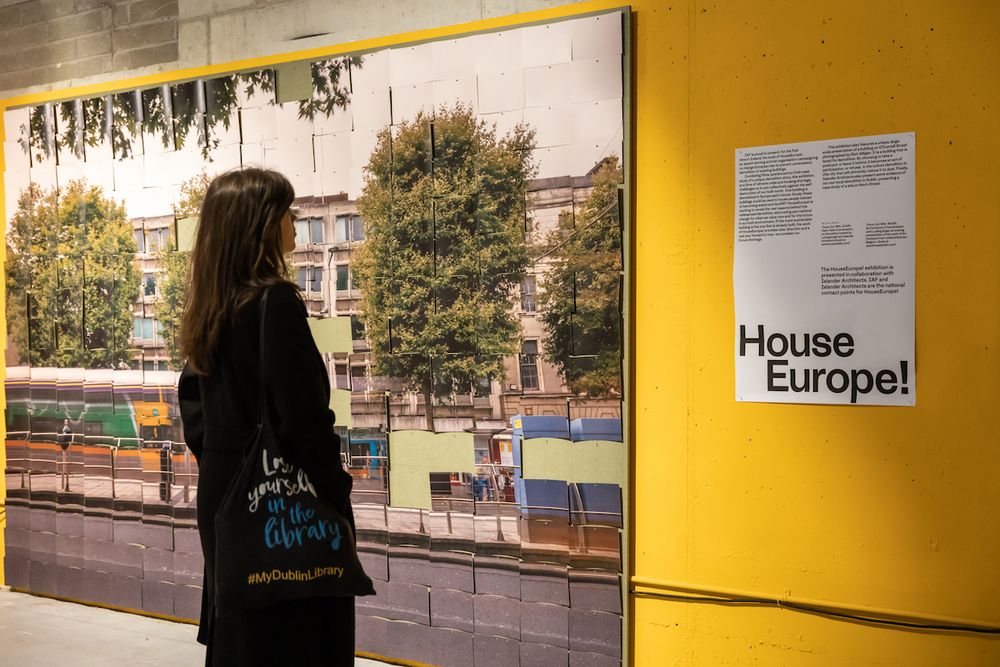 A young woman looking at a large-scale photo of O'Connell street on a bright yellow wall and the explanatory text for HouseEurope!