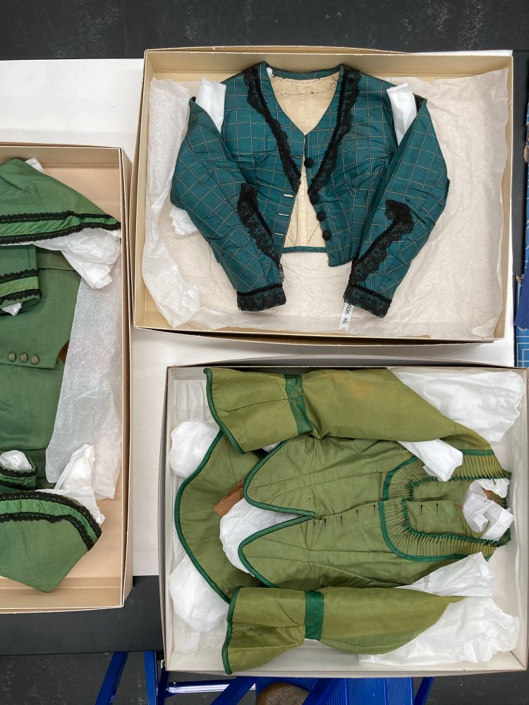 Three bodices of various shades of green laid in boxes on a table.