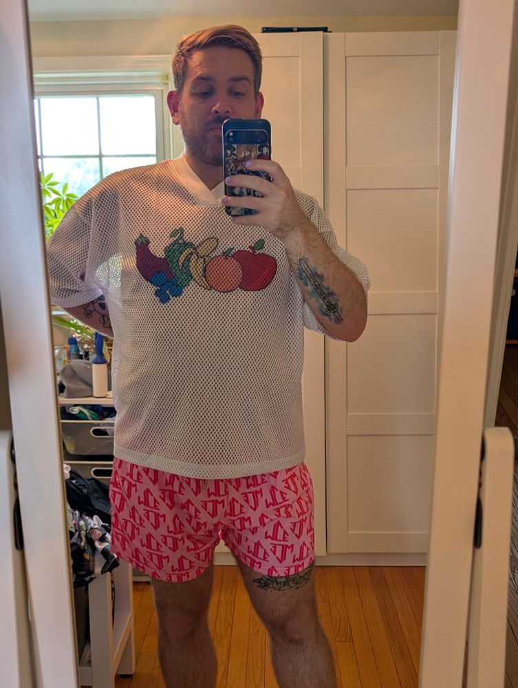 Selfie with mesh T-shirt with fruit images on the chest and pink swim shorts emblazoned with the MCE logo