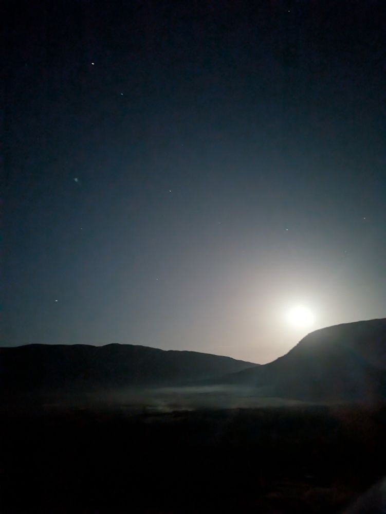 Full moon descending behind hill, mist in the valley, stars above
