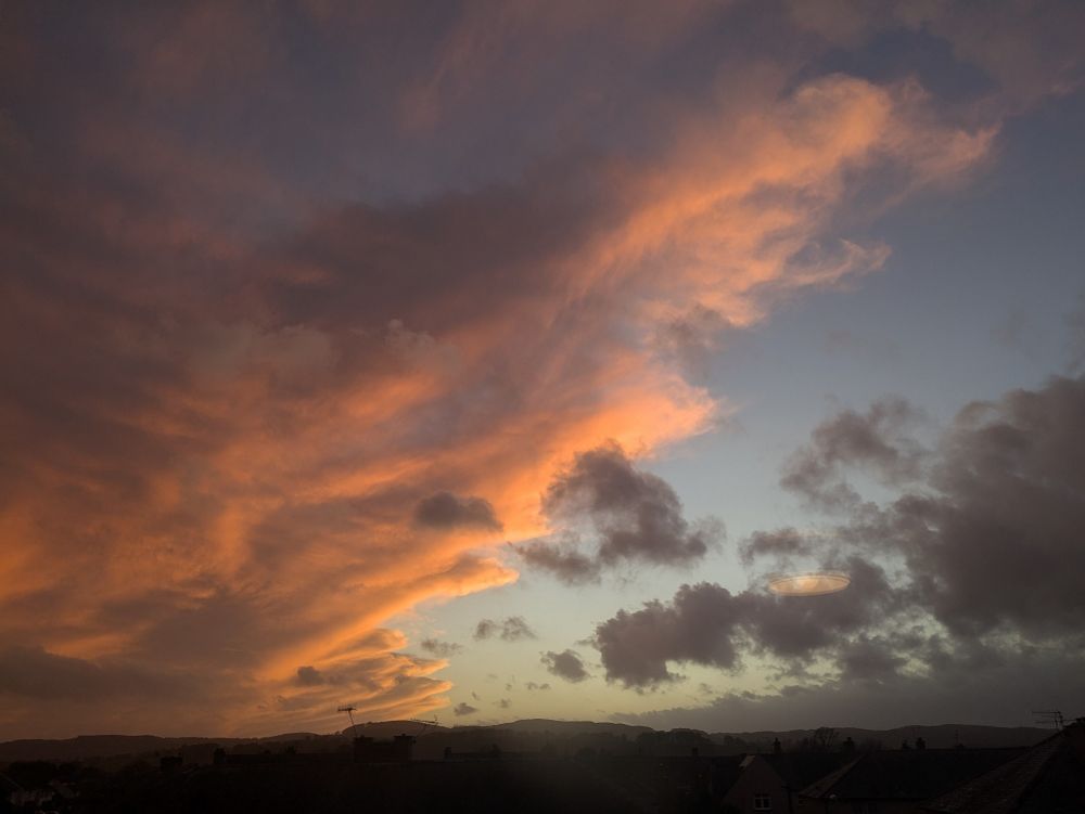 Ragged peach and grey clouds, strewn across a blue sky as the sun goes down.