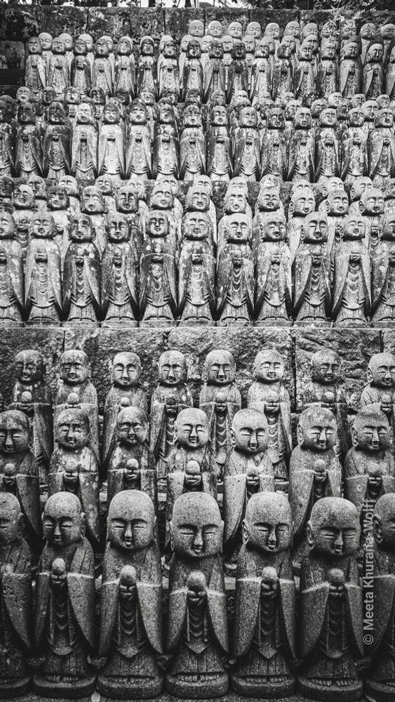 Rows upon rows of small stone Jizō statues stand solemnly at Hase-dera Temple in Kamakura, Japan. The statues, each carved with serene expressions and folded hands, represent guardians of children and travelers. Their weathered surfaces and uniform arrangement create a powerful sense of reverence, repetition, and quiet devotion amidst the temple’s moss-covered stone terraces. Image copyright Meeta K Wolff 