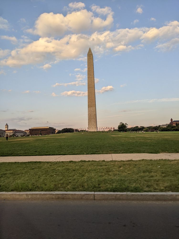 Picture of the Washington monument against a blue sky, taken from a distance on the road, without any people visible in the frame
