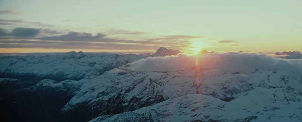 Fotograma de la película Las Dos Torres en el que se ve una cordillera escarpada llena de nieve y el sol despuntando al fondo.