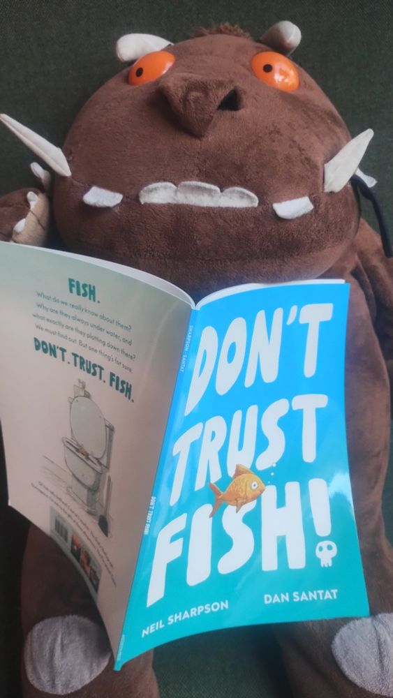 Cuddly Gruffalo plushie sitting and holding a copy of the picture book, Don't Trust Fish! in the Edinburgh Bookshop 