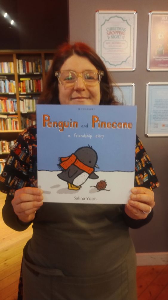 Bookseller Fiona holding up the picture book Penguin and Pinecone, in the Edinburgh Bookshop 