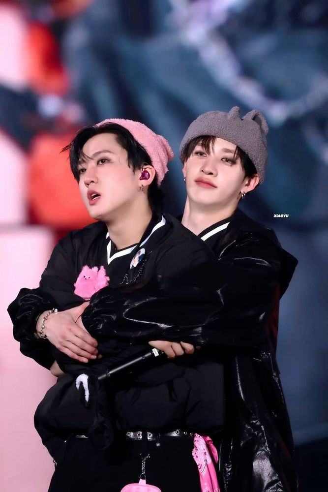 A photo of Bang Chan hugging Changbin from the back. They're each wearing hats of their respective SKZOO characters. 