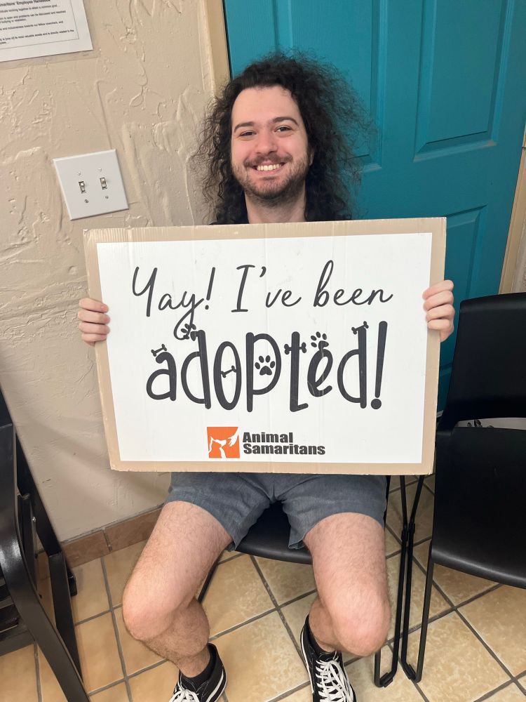 a photo of me smiling and holding a sign from an animal shelter that says “Yay! I’ve been adopted!”
