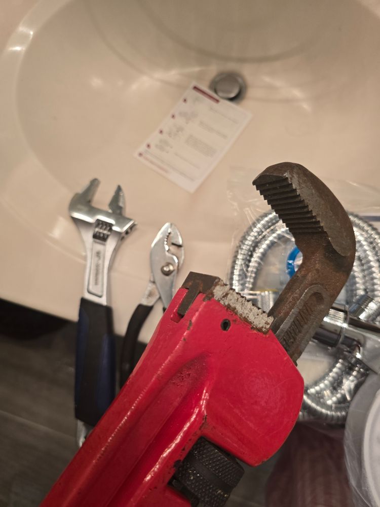 A medium crescent wrench next to plyers are overshadowed by a giant pipe wrench (I think that's what it is)