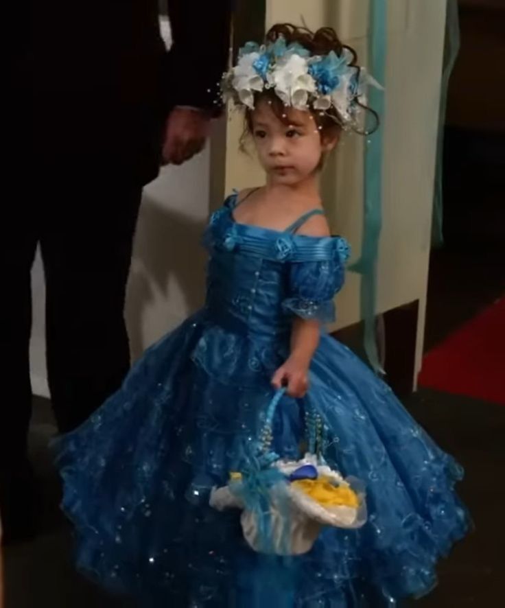 lily from modern family in a blue dress, holding a basket with her head cocked back
