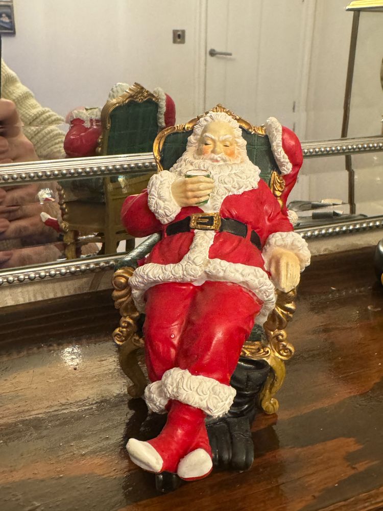 Image of a Christmas decoration of Santa sitting in a gilded golden chair with his boots off. Sitting back and sleeping.
