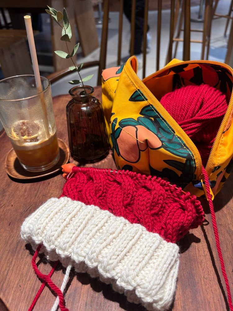 Santa hat with white ribbing and some progress on cables in red on a cafe table