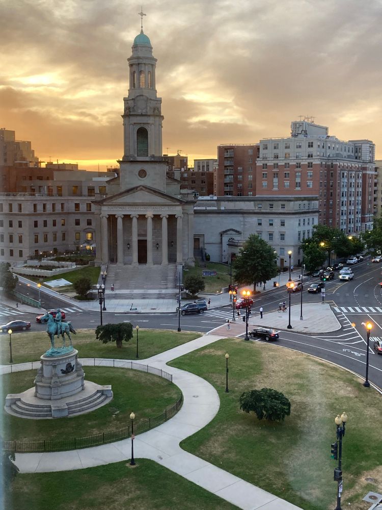 A photo looking out at a statue of George Henry Thomas and the surrounding traffic circle, with a church and the sun setting behind it. 

