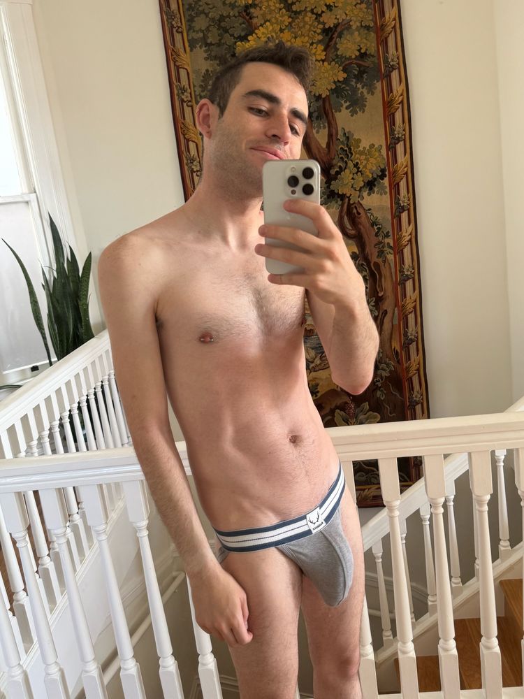 Standing in front of a mirror with my bulging cock barely contained by a jockstrap.