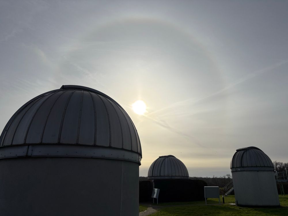 With severeal telescope domes in the foreground, there is a large circular halo around the Sun. The halo is approximately twice the size of an outstretched hand at arm's length. 