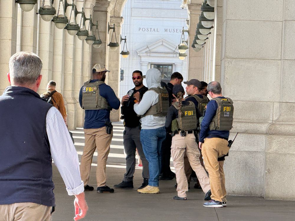Photo of a group of at least 7 people wearing flak jackets labeled “FBI”, standing outside a doorway to Union Station 