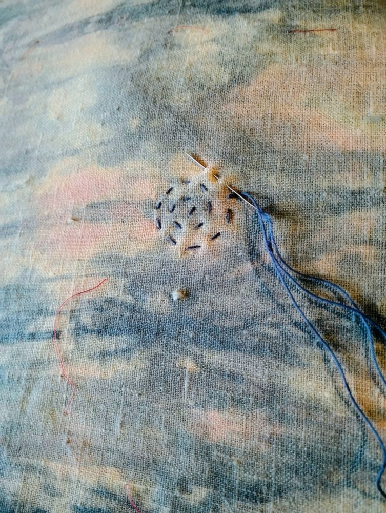 Coarse linen, marbled blue and ecru, a needle holding blue thread.