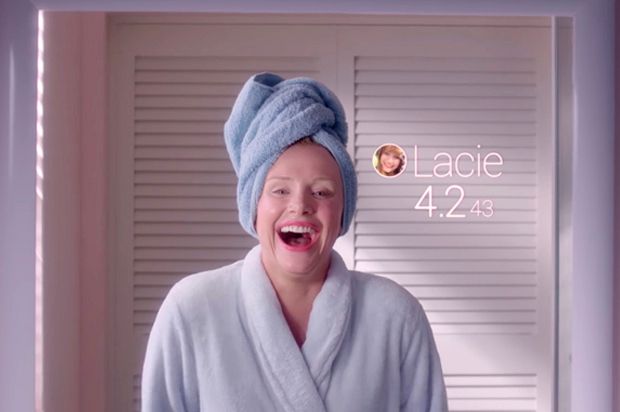 A still from the 2017 Black Mirror episode “Nosedive” showing Bryce Dallas Howard smiling way too big in the mirror as her socially-generated “score” appears next to her face.