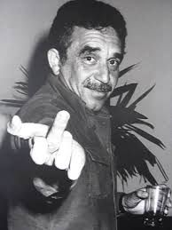 Foto em preto e branco do Gabriel Garcia Marquez levantando o dedo médio. Gabo tinha cabelo preto, bigode e te olha fixamente.