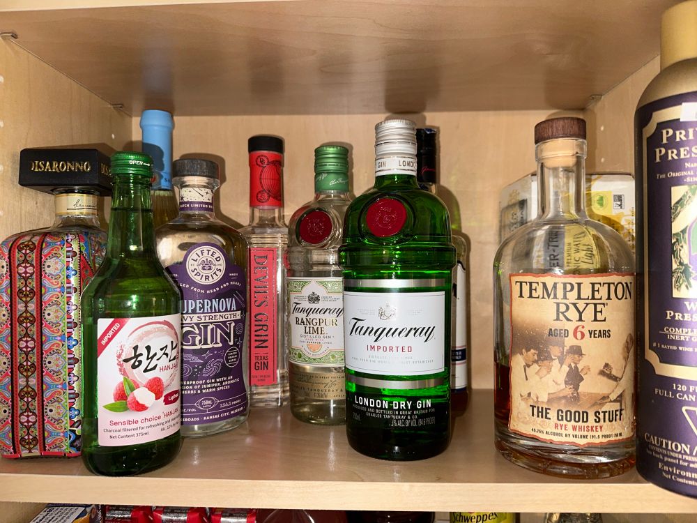 A cabinet shelf with 8 bottles of liquor, 1 fruit wine, a box of cans of Fever Tree less-sugar tonic, and pressurized gas for displacing oxygen in open bottles. 

Aside from the Templeton Rye, random Lychee drink, versace branded amaretto & KC Royals Jim Beam, I have basic Tanqueray gin, Tanqueray Rangpur Lime gin, Devil’s Spit gin from Texas and Supernova gin from KC. 