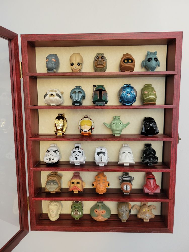 Multiple star wars character mini plastic heads are displayed in a wood curio cabinet