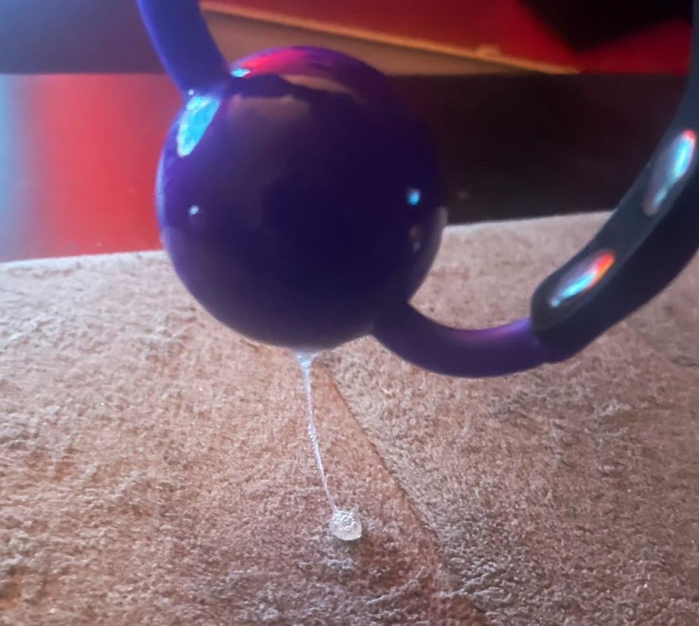 An image of a recently used purple silicone ball gag with saliva dripping from it.