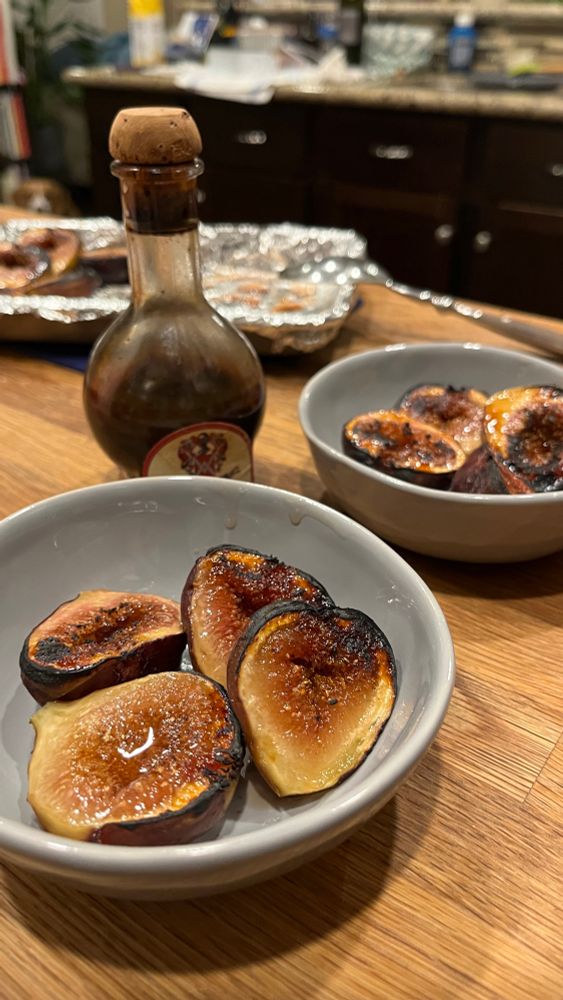 Broiled figs in small gray bowls and a bottle of aged balsamic in the background 