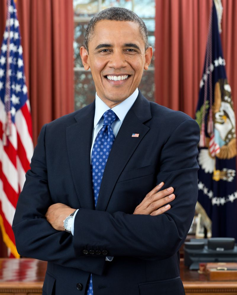 A picture of Barack Obama the 44th president in the Oval Office with his arms folded across his body.  He is smiling and looks very professional.